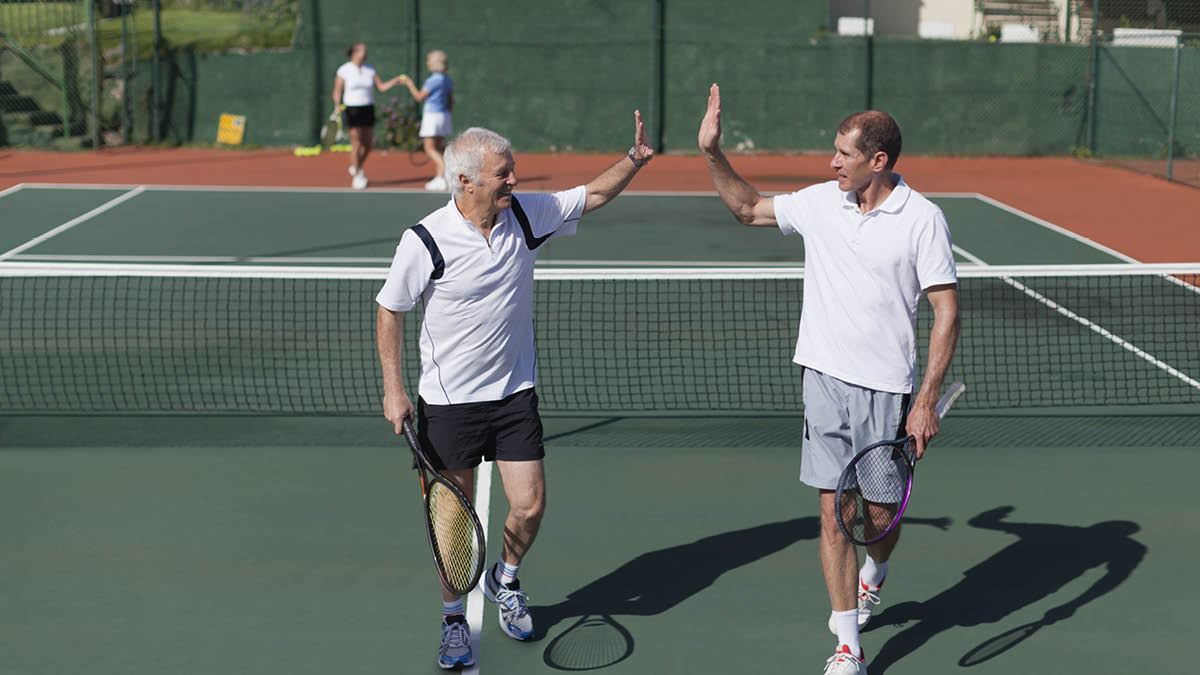 Two older men about to ‘high five’ on the tennis court.